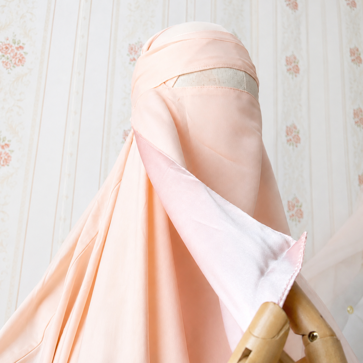 Mannequin wearing a pastel pink natural silk niqab, is lifting up the niqab to reveal the pure smooth shiny silk side of the niqab that is facing onto the skin. 100% silk niqab. Light pink silk lined niqab. 